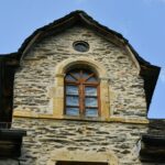 Close-up of a vintage stone building facade featuring wooden windows under a clear blue sky.
